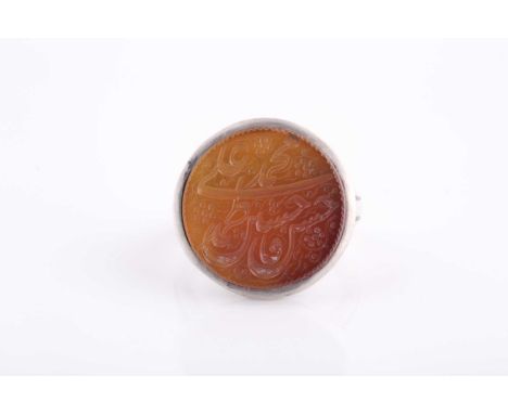 An Indo Persian white metal and orange stone ring, the circular stone engraved with calligraphy.