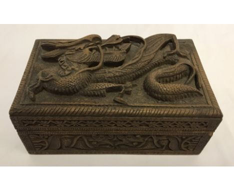 An ornately carved oriental wooden cigarette/trinket box. With deep carving of a dragon to lid, and dragon carvings to sides.