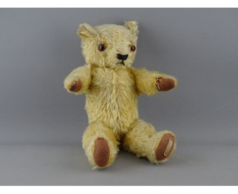 AN APPEALING BABY TEDDY BEAR, 30 cms long with glass eyes, stitched snout and sewn paws with original Chad Valley &amp; Co st