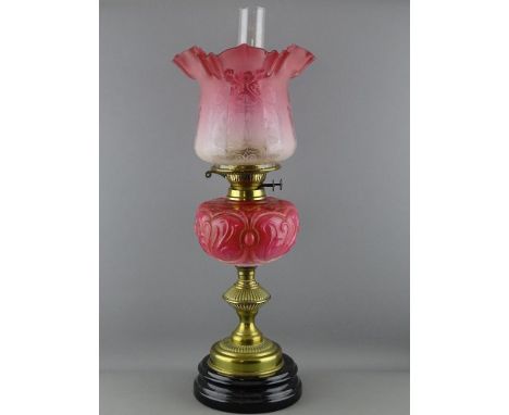 A VICTORIAN OIL LAMP with pink glass font and cranberry tinted shade on a baluster brass stem and circular pot base, the shad