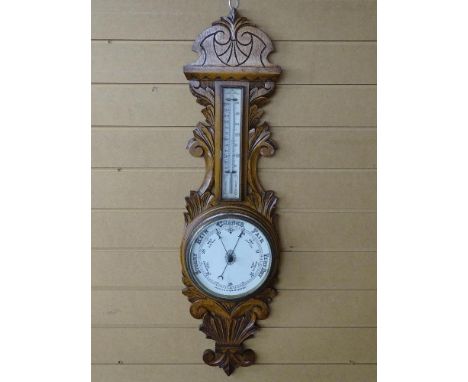 A VINTAGE ANEROID BAROMETER with ceramic dial and thermometer, set on a carved oak mount, 92 cms long