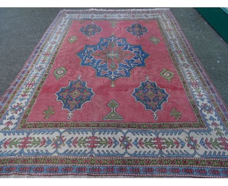 A PINK GROUND PERSIAN STYLE CARPET, classical style central pattern and multi-bordered edge with tasselled ends, 346 x 245 cm