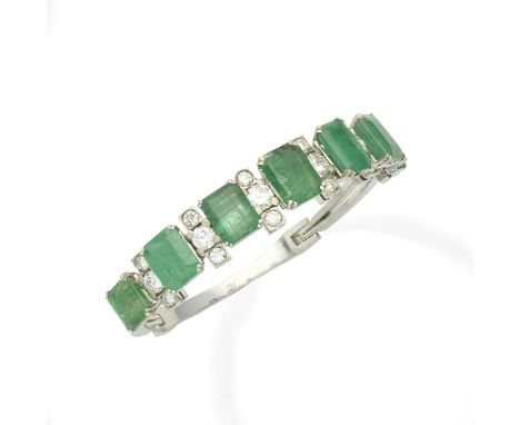 An emerald and diamond bangleSet to the front with a graduation of step-cut emeralds, accented by trios of brilliant-cut diam