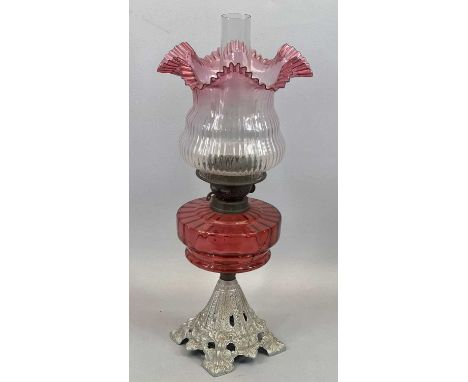 AN IRON BASED OIL LAMP - fine Cranberry glass reservoir and shade, 57cms total