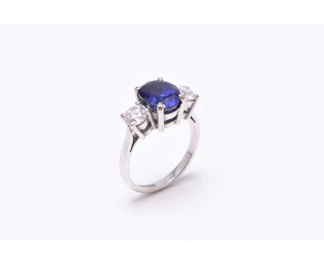 An 18ct white gold three stone sapphire and diamond ring, designed as a central oval mixed cut sapphire flanked to each side 