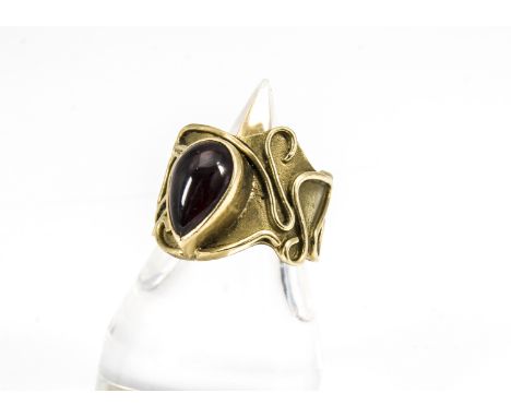 A contemporary 18ct gold garnet set dress ring, the shaped shank with sinuous applied trails centred with a pear cabochon cut