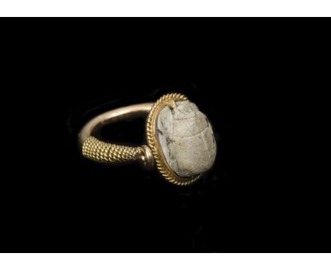 An archaeological revivalist ring, set with scarab carved top within a rope twist border on a torque stylised shank, ring siz