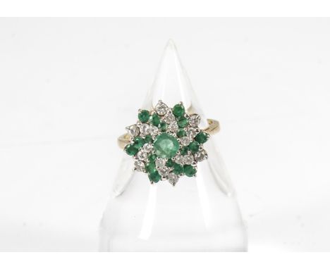 An 18ct gold emerald and diamond cluster ring, the central mixed cut circular emerald in claw setting surrounded by alternate