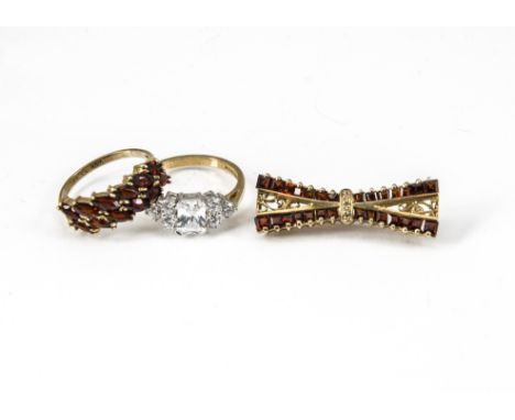 Two contemporary gem set dress rings, and a garnet and diamond bow tie brooch, the white stone dress ring on 9ct gold shank, 