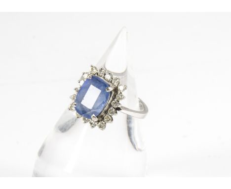 A sapphire and diamond cluster ring, the rectangular mixed cut pale blue sapphire in four claw setting surrounded by a diamon