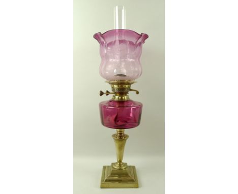 A Victorian brass and glass paraffin lamp with cranberry glass reservoir, and shade etched with roses in the William Morris s