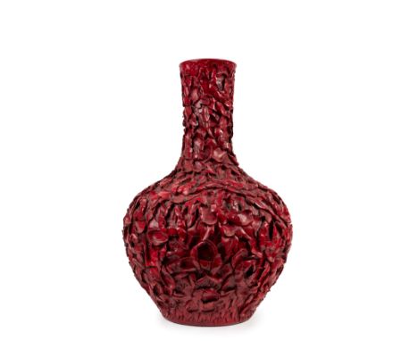 Finely decorated in relief across the entire body with flowers, it is completely covered in red glaze; on the base is the apo