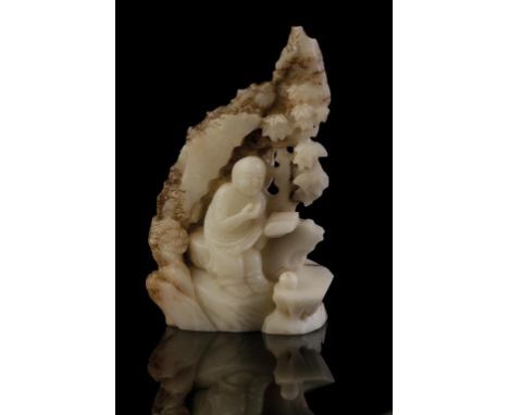 WHITE AND RUSSET JADE GROUP, QING DYNASTY, 19TH CENTURY, carved as a scholar reading a book, seated on a rocky outcrop, 13cm 