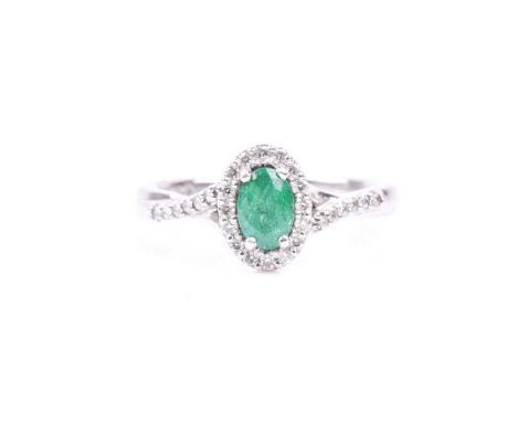 A platinum, diamond, and emerald cluster ring, set with a mixed oval-cut emerald, within a border of round brilliant-cut diam