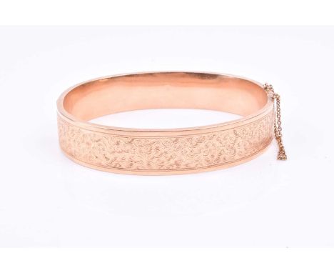 A yellow metal bangle bracelet, with engraved decoration, indistinct mark to clasp, internal diameter 6.3 cm, likely 9ct.Foot