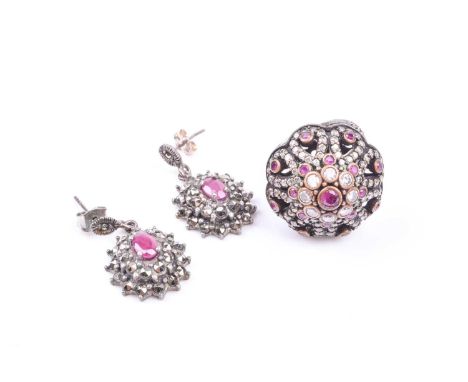 A silver, ruby, and white gemstone domed ring, collet-set with round-cut stones, with scrolled decoration to shoulders, marke