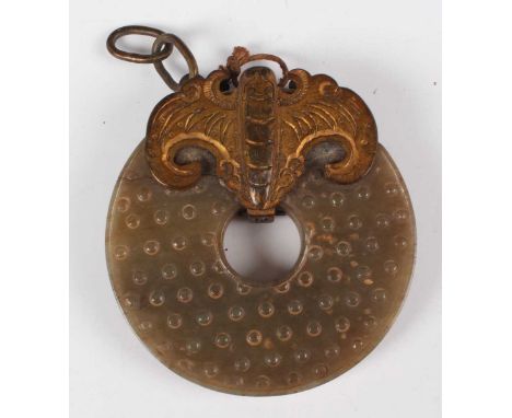 A Chinese archaistic jade bi disc, carved in low relief with a rice grain design, the stone of pale brown and green mottled t