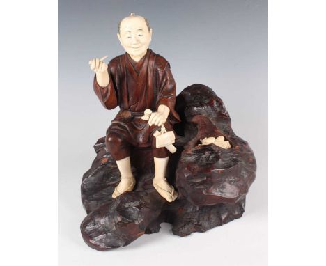 A Japanese carved wood and ivory okimono figure group, Meiji period, modelled with a gentleman seated on a rocky outcrop, inl
