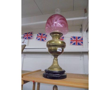 A late Victorian brass oil lamp on ceramic base with Victorian cranberry glass shade, in good condition.Brass lamp is dusty &