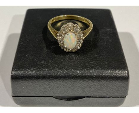 An 18ct gold opal and diamond flowerhead cluster ring, size M, the central polished oval opal cabochon surrounded by ten bril