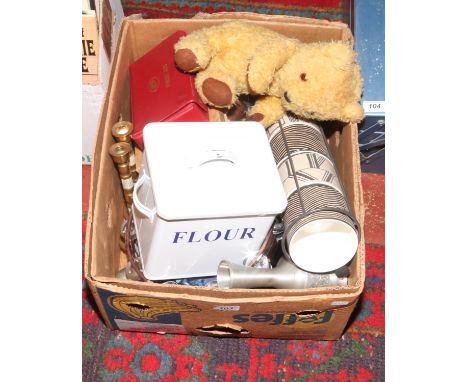 A box of household items including an enamel flour bin, teddy bear, tambourine and candlesticks.