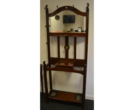 An Arts and Crafts, mahogany hall stand, arched mirror over shelf amid shaped metal hooks, hinged cover to glove box flanked 