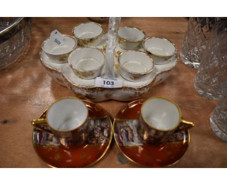 A vintage ceramic egg cup holder and two cabinet cups and saucers depicting classical scene.