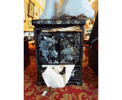 An Oriental lacquered mother of pearl inlaid table top cabinet fitted with a pair of doors over a single drawer and raised on