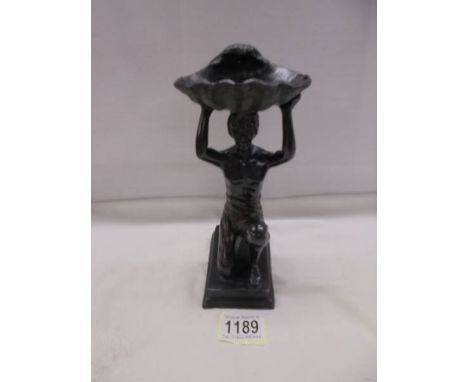 A bronze figure of a kneeling man holding a large shell above his head.