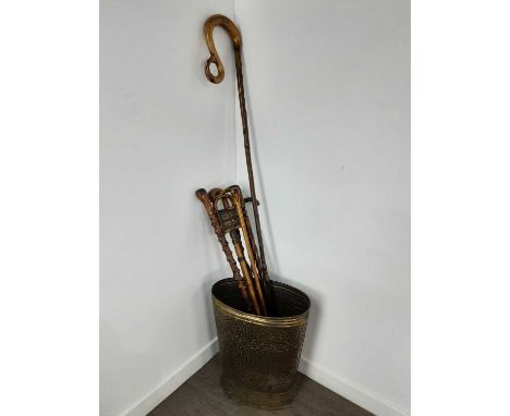 BRASS STICK STAND, LATE 19TH / EARLY 20TH CENTURY of tapered oval form, embossed decoration, with a selection of hardwood wal