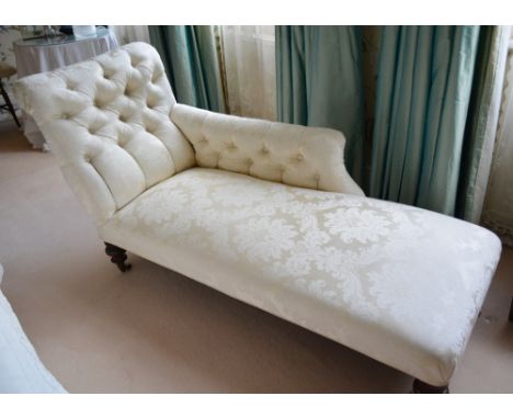 A Victorian Chaise Longue, with a button upholstered scroll end and cream damask upholstery raised upon low turned feet with 