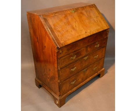 A George I Walnut Bureau, the herring banded fall front enclosing a fitted interior with various alcoves and drawers with cen
