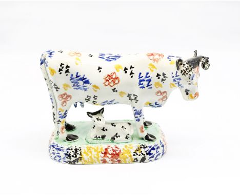 A Prattware cow standing on an oblong base, with her calf laying recumbent beneath her. Sponge decorated in multi coloured en