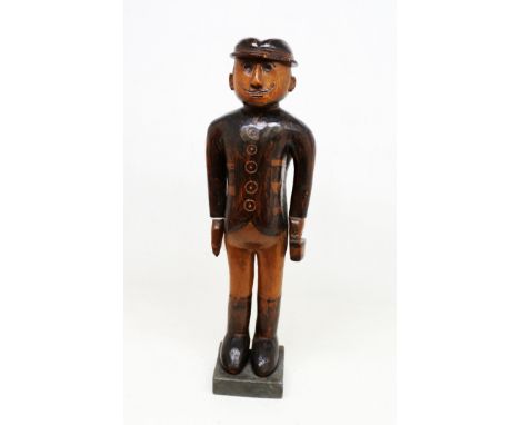 An early 20th century Folk Art figure of a gentleman, in hat and tailored suit, trousers and boots, carrying a box in left ha