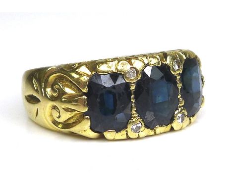 An 18ct gold three stone ring, set with oval cut dark blue stones, central 7.4 by 5.7 by 2.4mm, and four small white stones, 