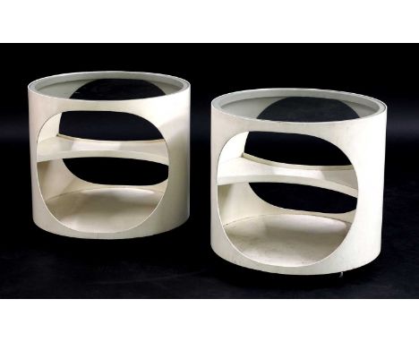 A pair of white painted side tables,each of cylindrical form, with a glass top, cut-out sides with a shaped shelf, on castors