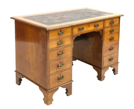 An Arts and Crafts walnut desk,with an arrangement of eleven drawers, losses to the leather top, raised on high arabesque bra