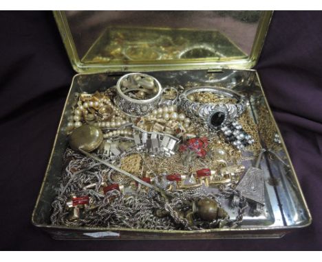 A vintage tin containing a selection of costume jewellery including chains, bangles, cufflinks etc