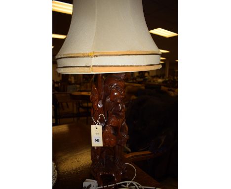 A modern carved wooden table lamp in the form of an Oriental deity, fitted with a cream coloured shade.
