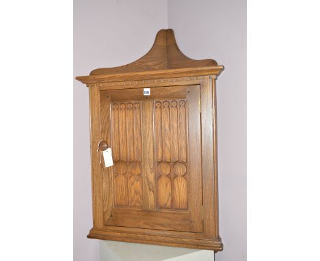 An Ercol elm hanging corner cabinet with carved panelled door.