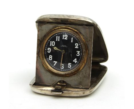 A silver cased travelling bedside clock, the circular black dial with Arabic numerals and luminous hands, the silver case wit