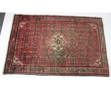 A Hamadan rug with central medallion and surround of geometric designs on a red ground within a multi figured border, 213cm x