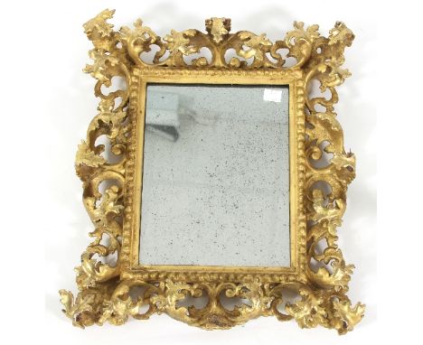 A Florentine giltwood mirror with elaborate pierced scroll and foliate surround within a beaded border, fitted a rectangular 