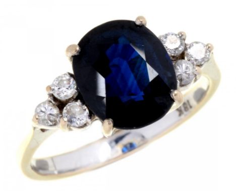 A SAPPHIRE AND DIAMOND RING  the larger cushion shaped sapphire between triple diamond  shoulders, in white gold marked 18 K,