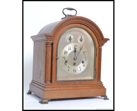 An 20th oak cased mantle clock, having a silvered face with two subsidiary dials, with three-train movement striking on a coi