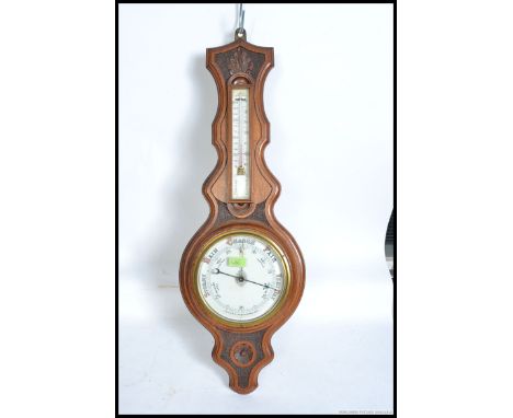 A 1920's oak aneroid banjo barometer. The carved oak frame with ceramic faced barometer and thermometer.
