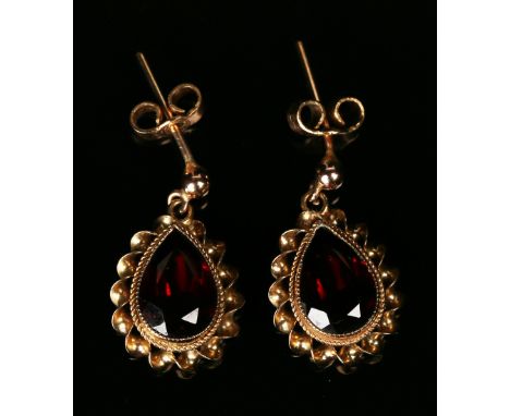 A pair of 9ct gold and garnet single stone earrings, each mounted with a pear shaped garnet within a ribbon twist surround, w