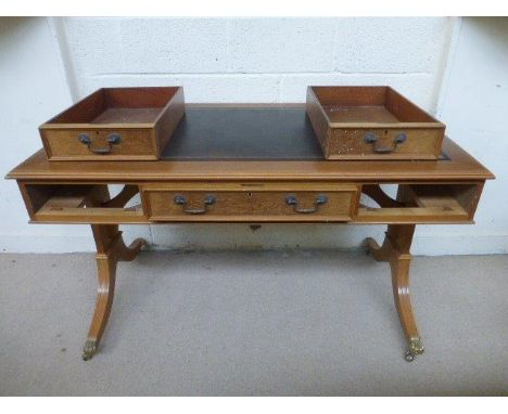 A contemporary light oak leather-topped desk with three drawers raised on swept supports to lion paw brass castors, probably 