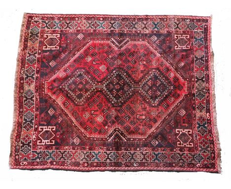 Middle Eastern carpet, the brick red ground with triple lozenge pattern centre surrounded by multiple borders and tasselled e