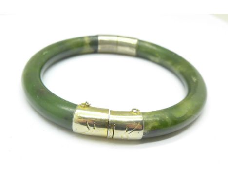 A jade bangle with white metal fittings 